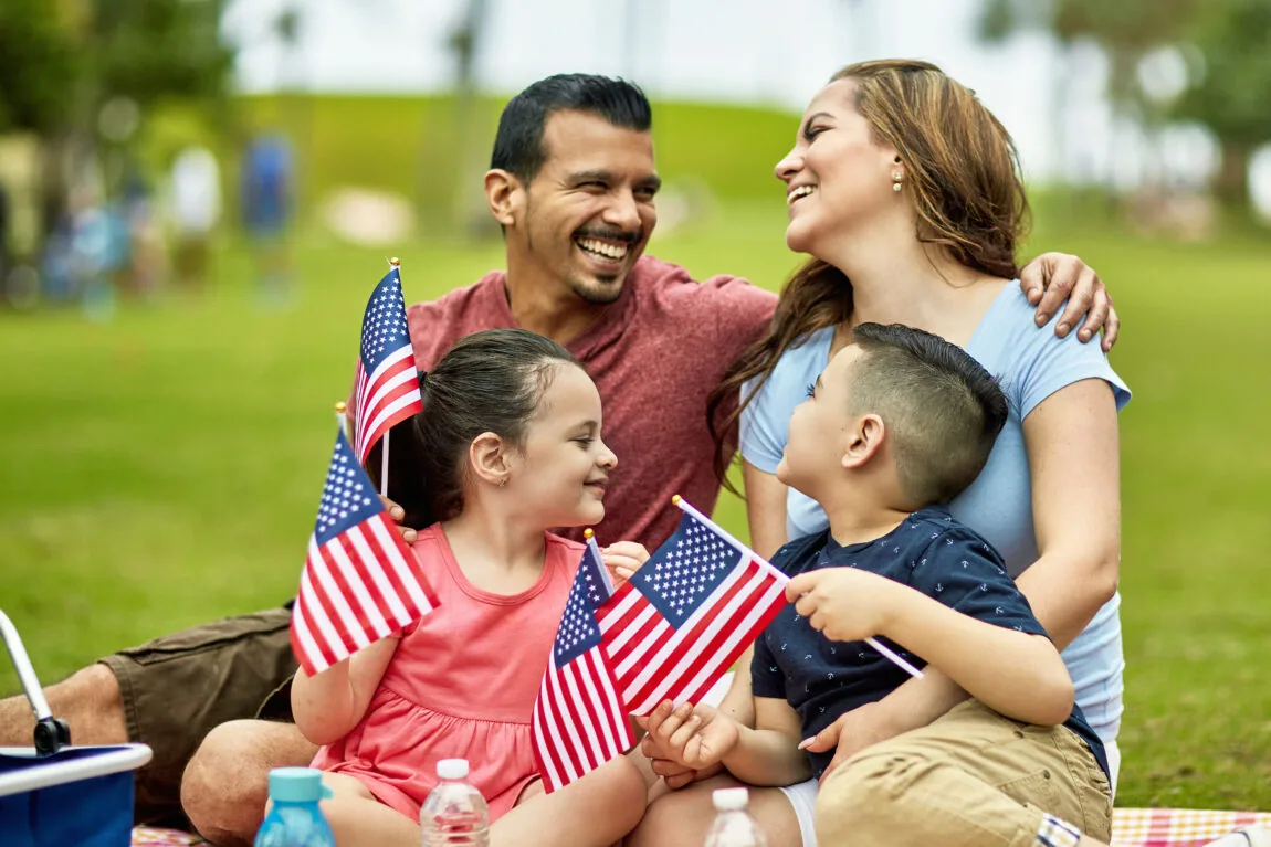 Smiling family with young children holding American flags at a park